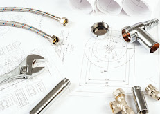 Plumbing tools, pipes, and blueprints laid out on a table.